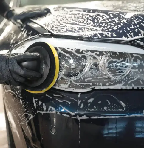 Man cleans car lamp with circle sponge. Preparing auto for polishing. 
Detailed car wash